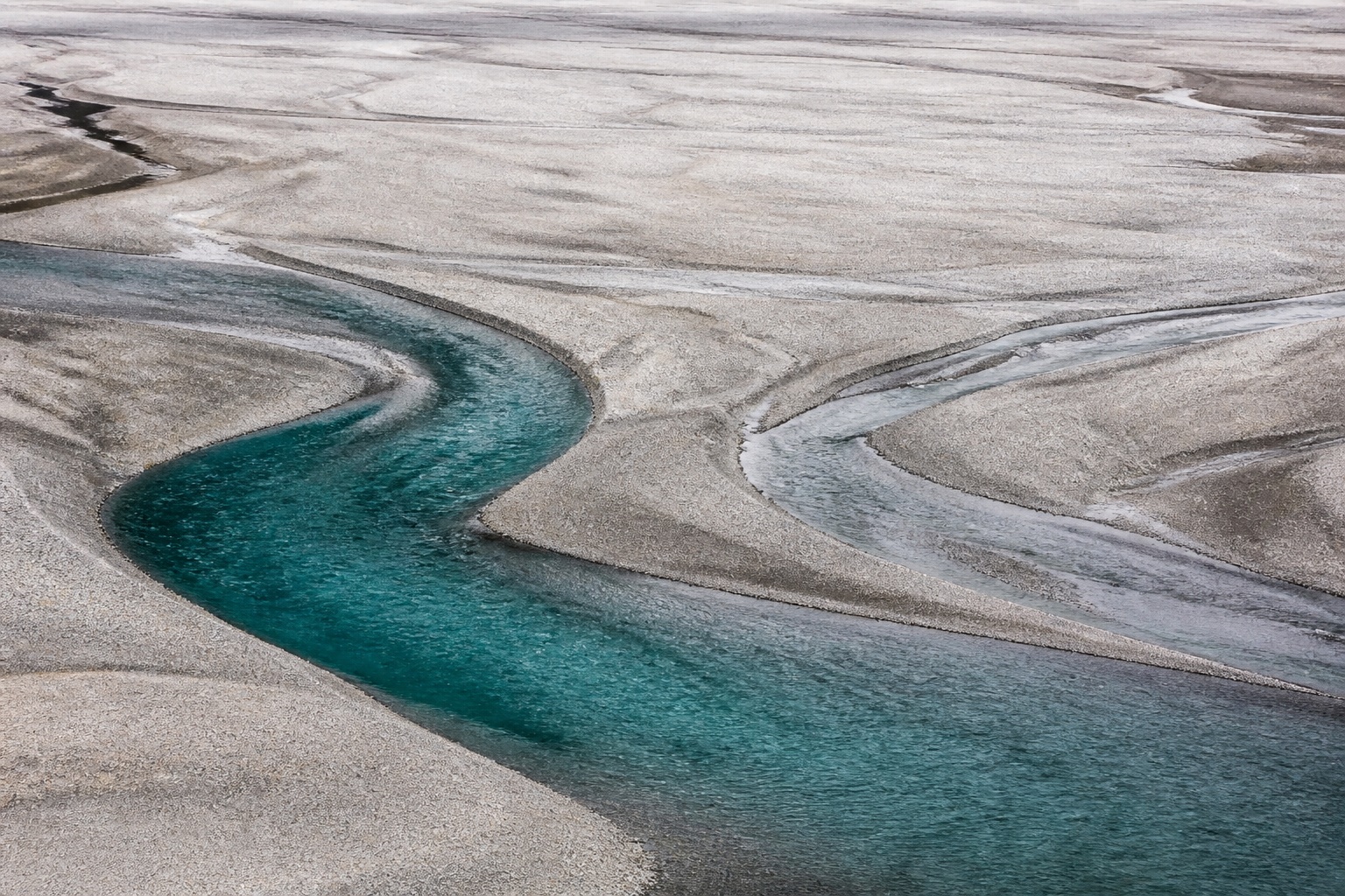 Two curving river channels cross a pale gravel plain.